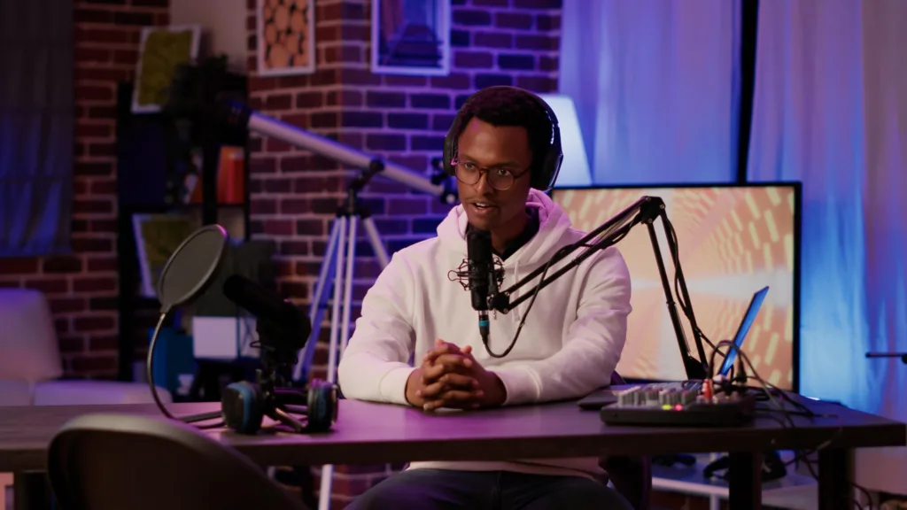 portrait-african-american-podcaster-adjusting-digital-audio-mixer-while-talking-live-audience-using-microphone-male-online-radio-host-smiling-confident-camera-while-recording-home-studio