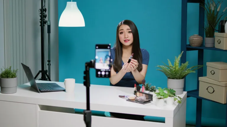 content-creator-doing-product-review-camera-studio-filming-video-with-makeup-cosmetics-female-influencer-recording-lipstick-recommendation-vlog-with-smartphone-social-media