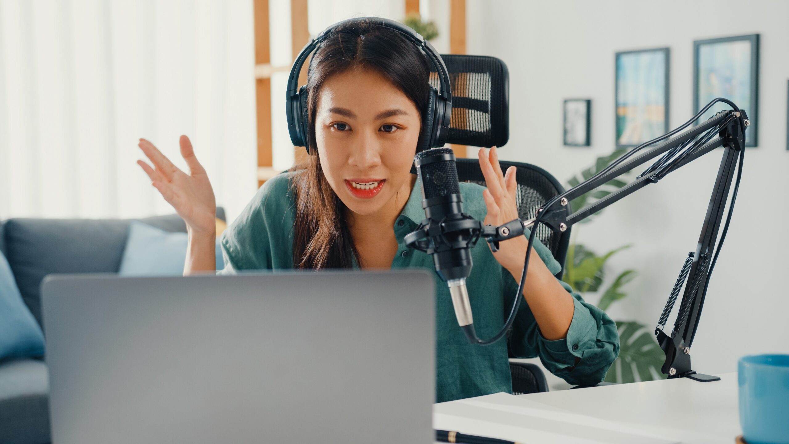 Happy Asian girl recording a podcast on her laptop computer with headphones and microphone