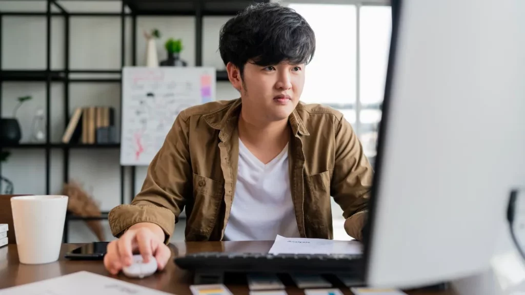 Person working at a desk with a computer, mouse, coffee cup, and papers in a modern office setting.