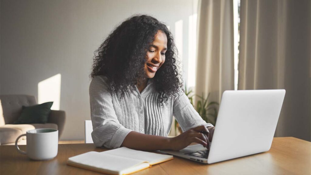 a smiley woman typing something on her laptop