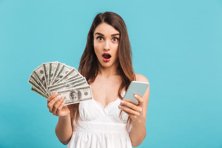 a shocked young woman with money and a phone