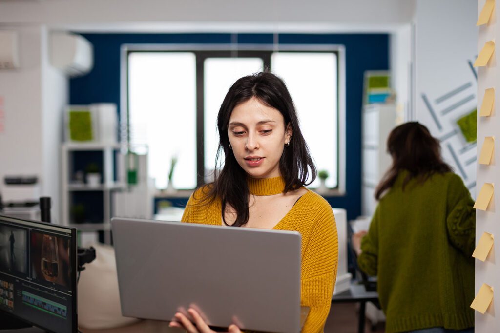 woman editing video on laptop while standing