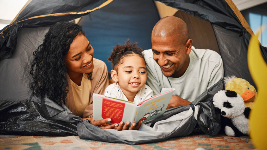 home camping and a child reading a story book with their parents