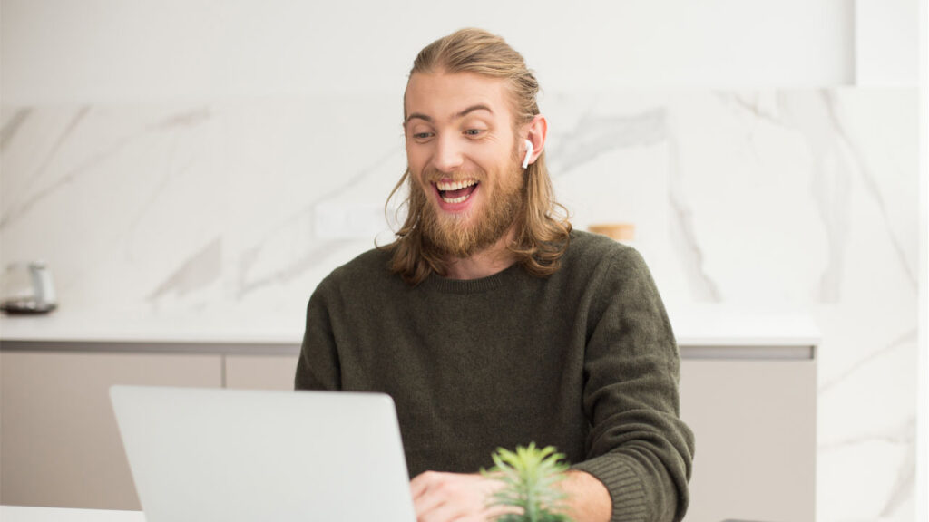 man in earphones sitting at the table with laptop at home laughing