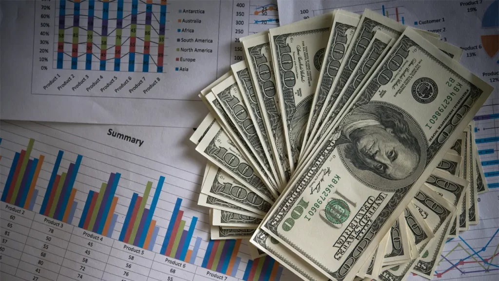 Dollar notes on a pile of spreadsheets.