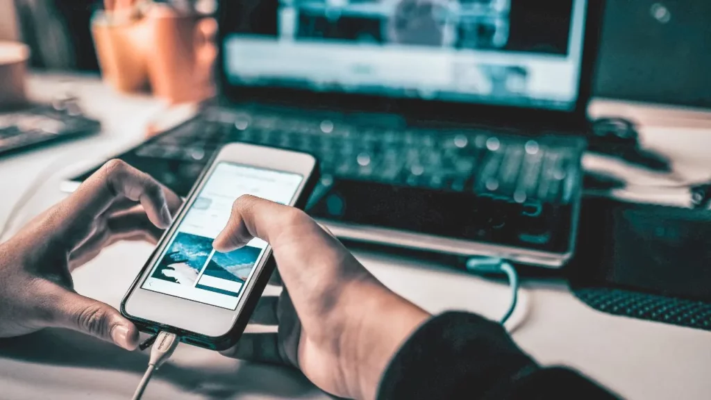 Person using a phone with a laptop in the background.