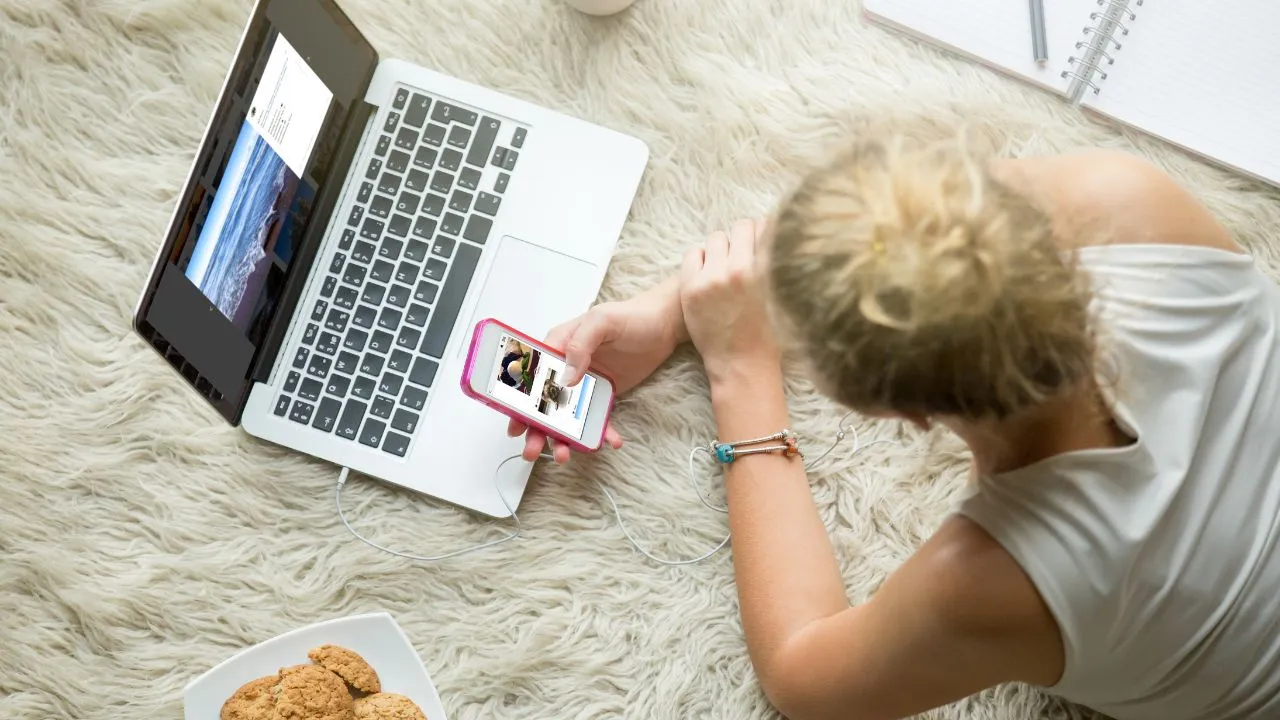 Woman using laptop and phone on a cozy rug.