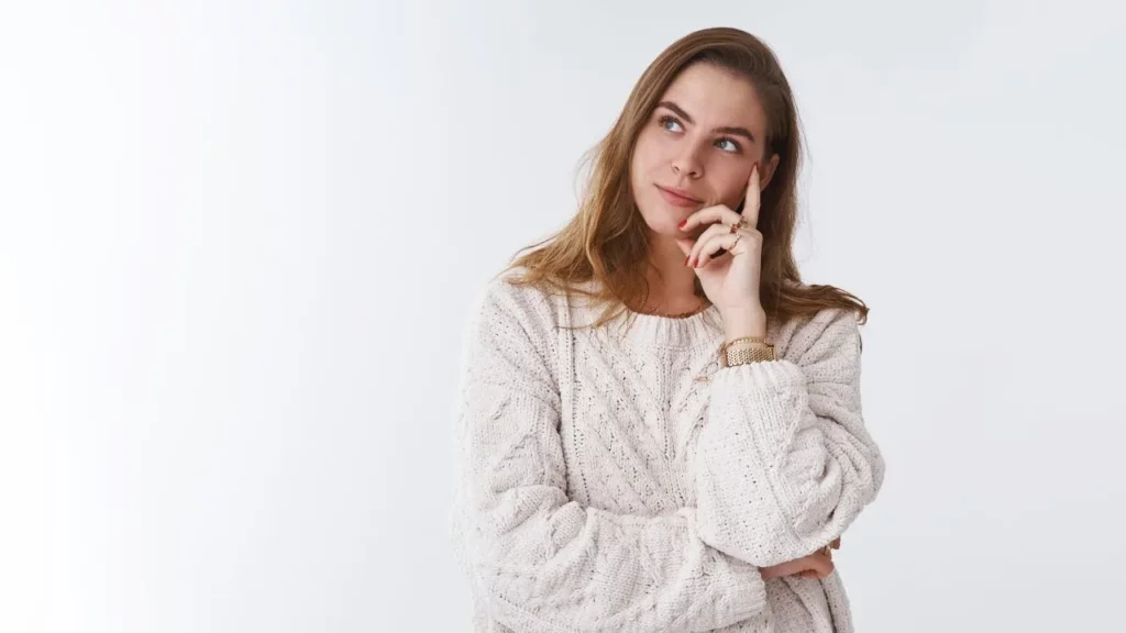 Woman thinking with hand on chin against a plain background.