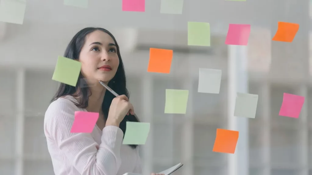 Woman in office holding pen with colorful sticky notes in background.