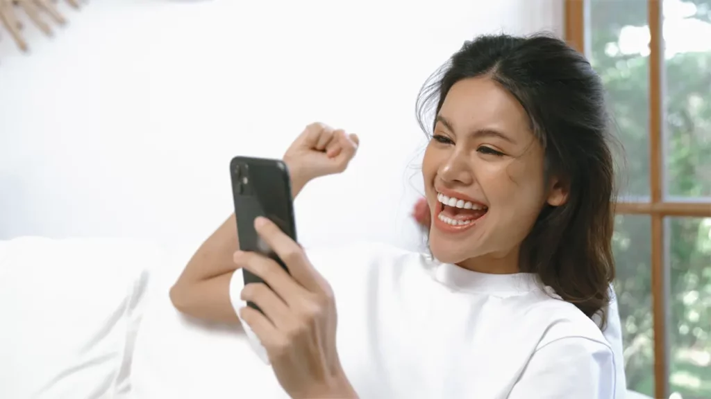 A woman cheering while on her smart phone.