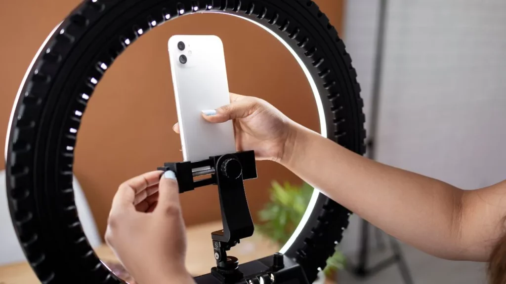 A person's hands adjusting a smartphone in a ring light, showing a typical setup for creating video content.