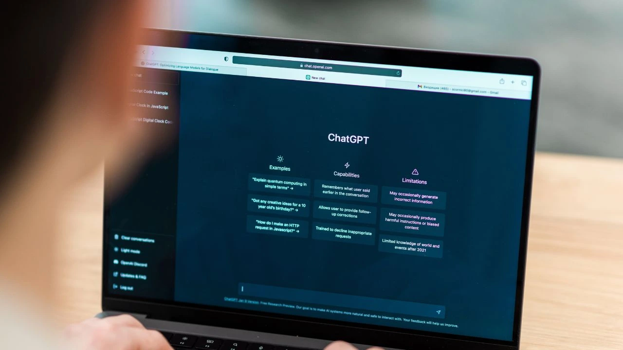 Person using a laptop to access ChatGPT website with examples, capabilities, and limitations displayed.