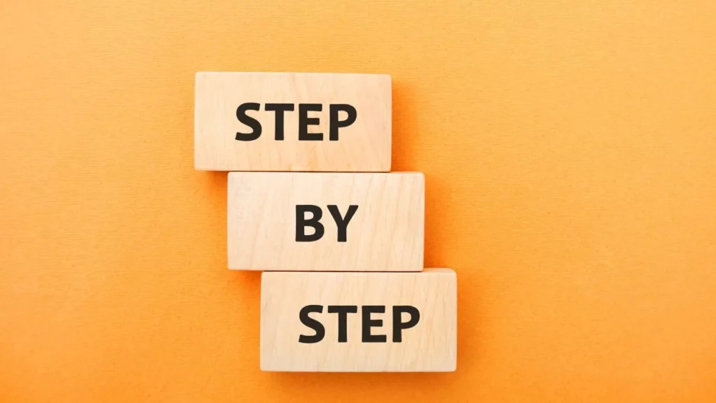 Wooden blocks spelling "STEP BY STEP" on an orange background.