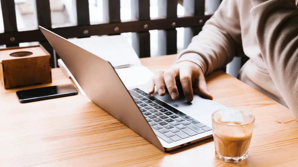 Person working on a laptop with a coffee cup on a wooden table in a cozy setting.