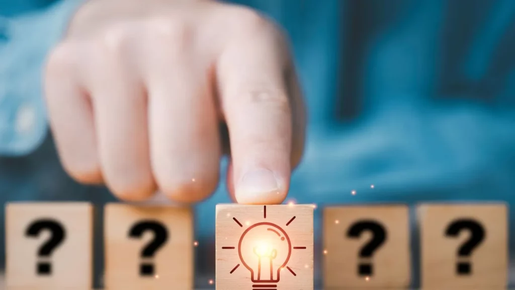 A hand placing a wooden block with a lightbulb icon among other blocks with question marks.