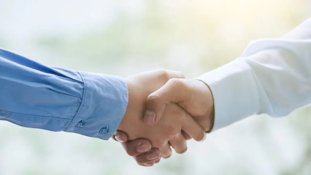 Two hands in business attire shaking in agreement against a blurred outdoor background.