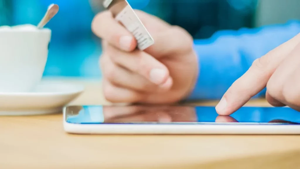 A person holding a credit card while tapping on a smartphone screen at a table.