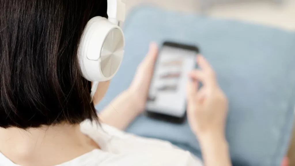 Person wearing white over-ear headphones while scrolling on a smartphone, viewed from behind.