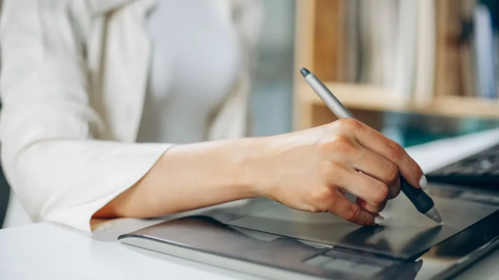 Close-up of a person’s hand using a stylus on a digital drawing tablet.
