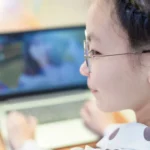 Young girl with glasses and braids focused on a laptop screen.