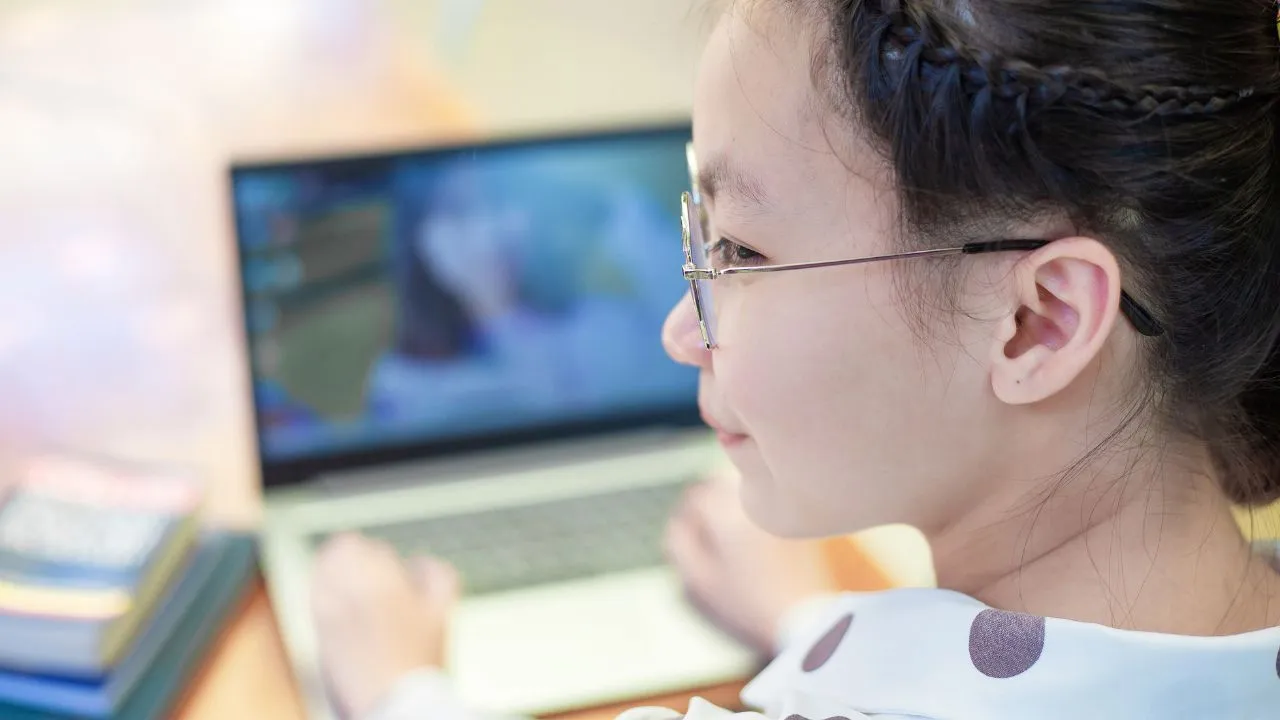Young girl with glasses and braids focused on a laptop screen.