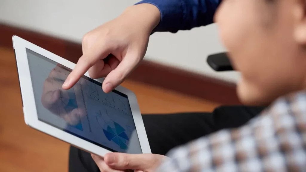 A close-up of a person's hands pointing at colorful data charts on a tablet screen.