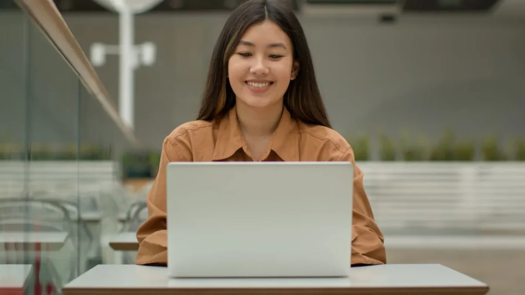 A smiling woman focused on her laptop in a bright, modern workspace.