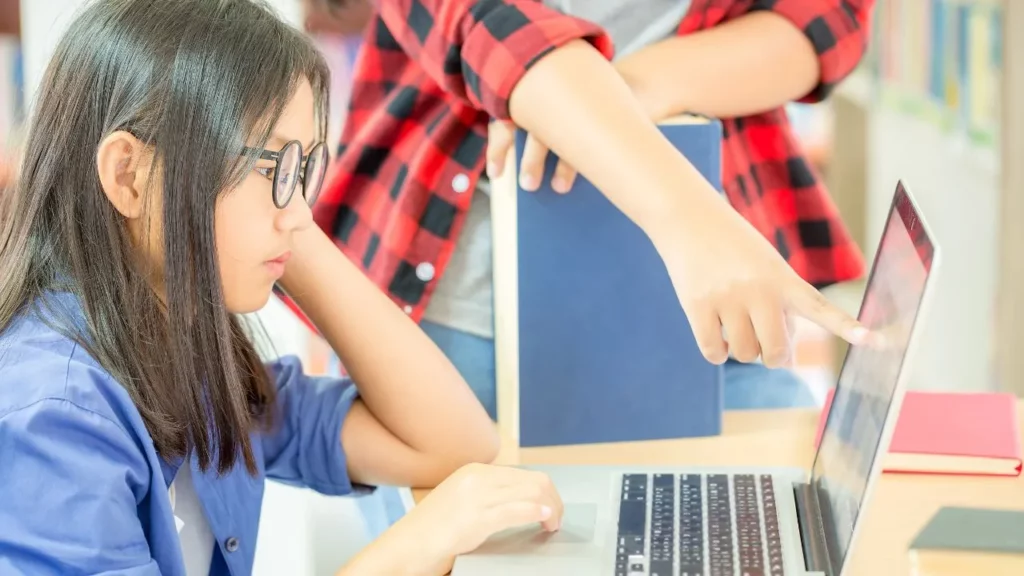 A student receiving guidance while working on a laptop in a library.