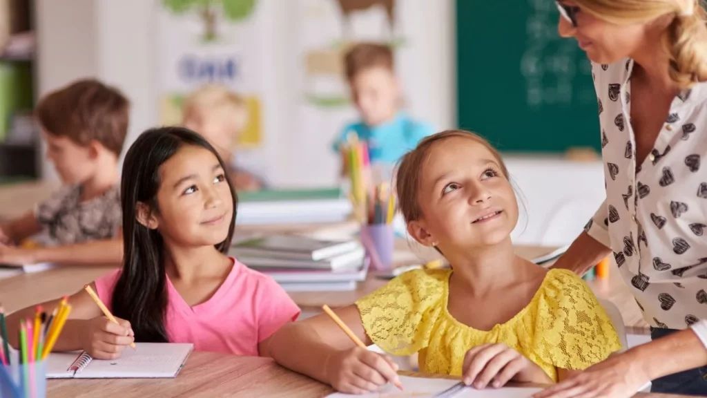 Two young students looking up and smiling at their teacher during a lesson.