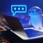 A 3D-rendered white robot wearing glasses sits at a laptop with a glowing blue speech bubble above its head.
