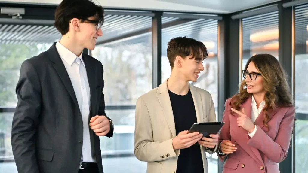 Three colleagues in business-casual attire standing and talking while holding a tablet.