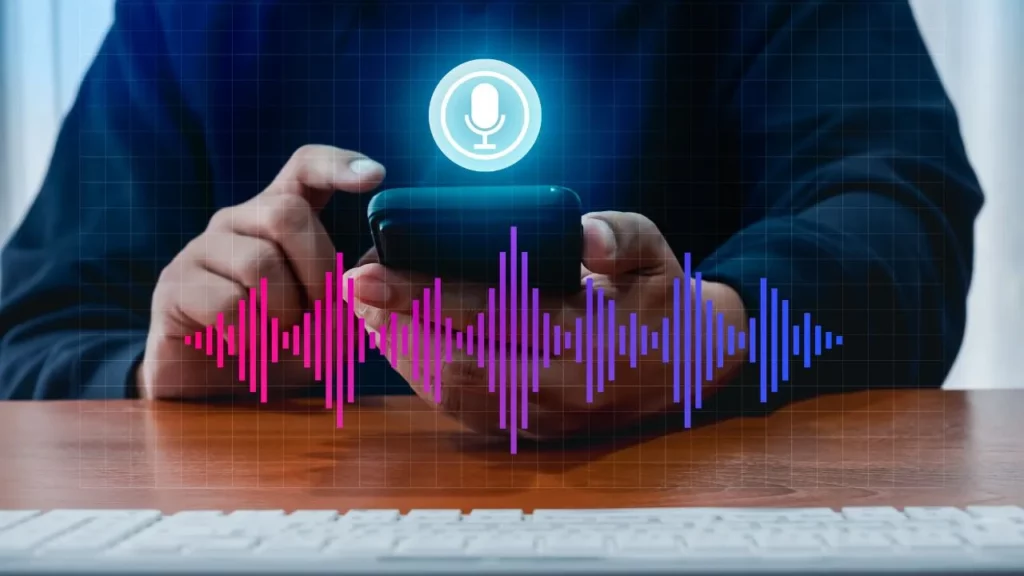 Close-up of a person holding a smartphone with a glowing microphone icon and a colorful digital sound wave overlay, representing voice recognition or audio processing.