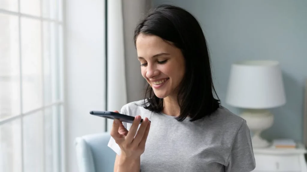 A smiling woman holding her smartphone horizontally while using voice commands or the speakerphone.