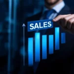 A businessman pointing to a glowing blue bar chart and a "SALES" button with an upward arrow.