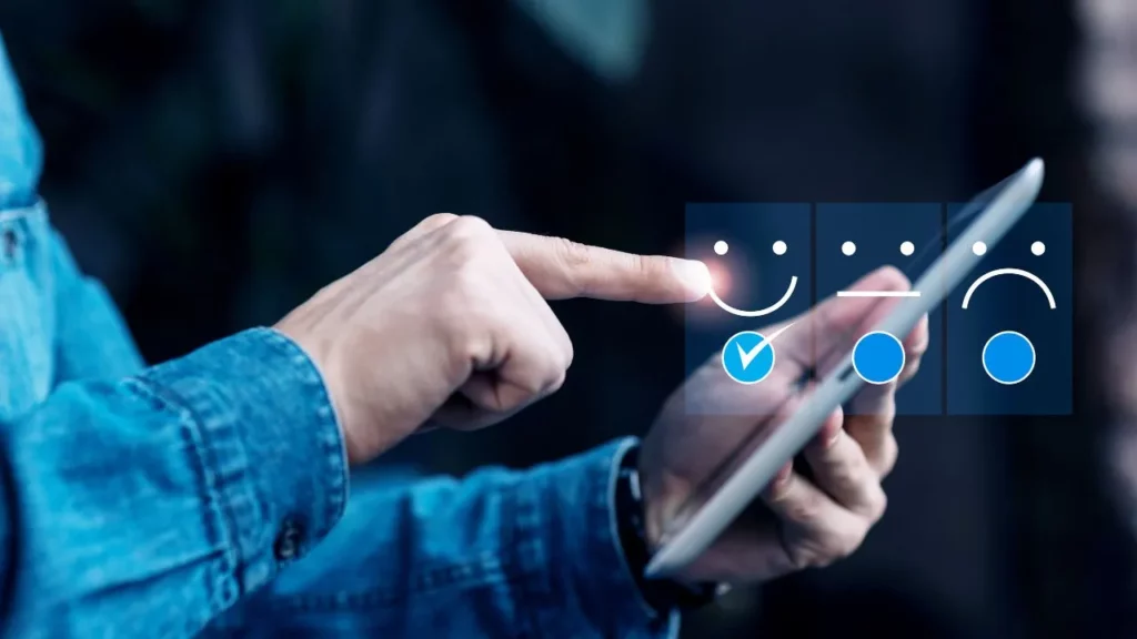 A person in a denim shirt using a tablet to select a happy face icon from a digital feedback survey.