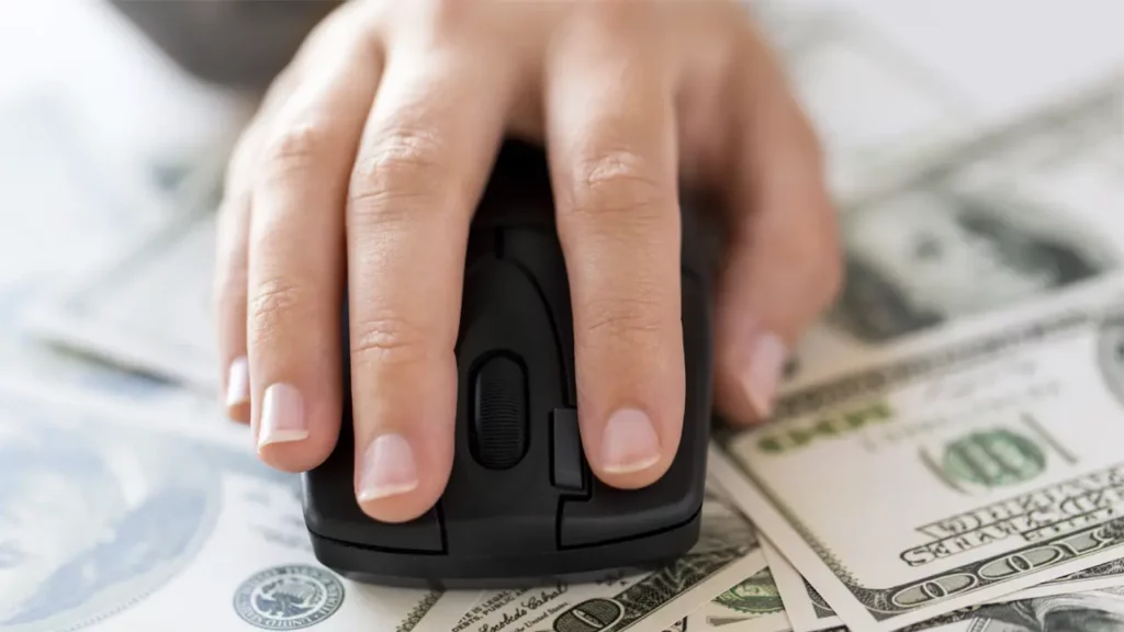 Someone using a computer mouse on a pile of dollar bills.