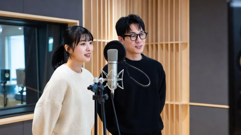 A woman in a white sweater and a man with glasses standing together in a recording studio.