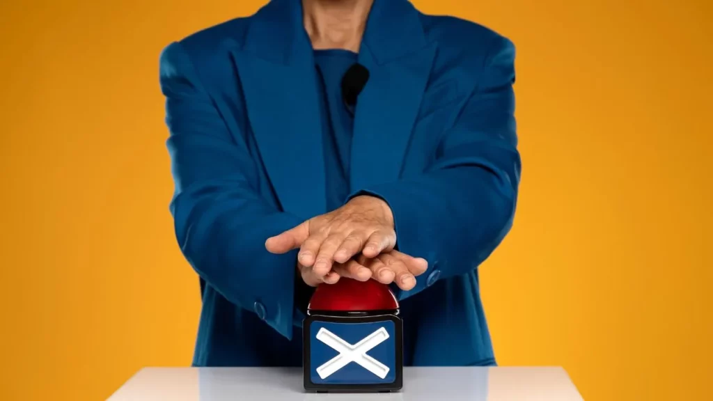 A person in a blue suit prepared to press a large red buzzer with a white "X" on it.