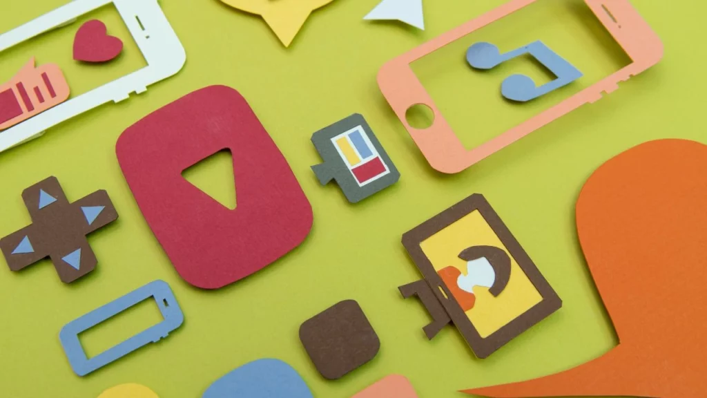 Colorful paper cutouts of various social media, video, and music icons scattered on a green surface.