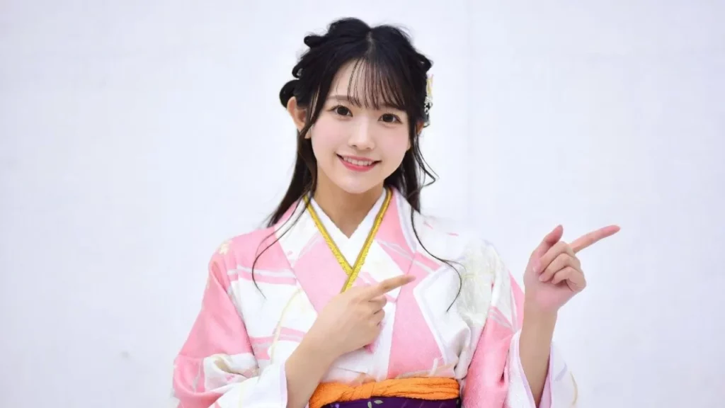 A smiling young woman in a pink and white kimono pointing toward the side against a white background.