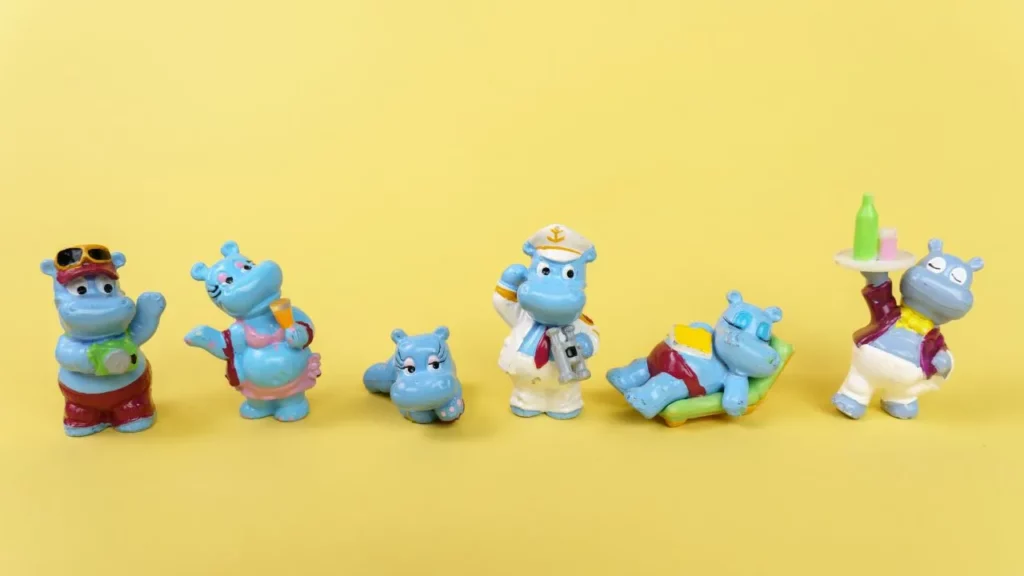 A row of six small, blue plastic hippopotamus figurines in various vacation-themed outfits and poses against a yellow background.
