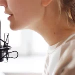 Close-up side profile of a person speaking into a black studio microphone.