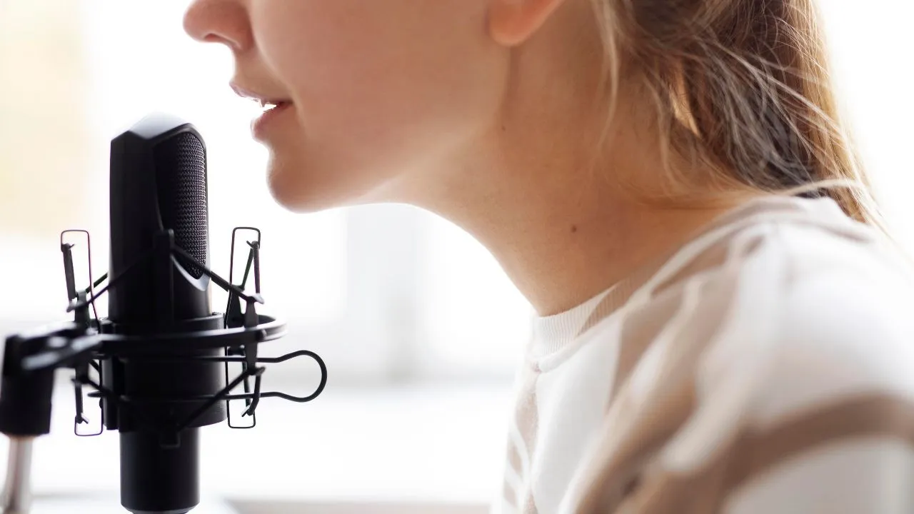 Close-up side profile of a person speaking into a black studio microphone.